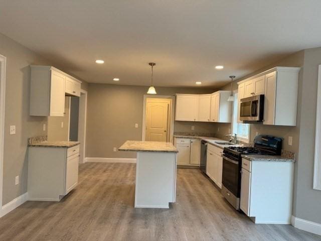 kitchen featuring appliances with stainless steel finishes, a center island, light wood-style flooring, and baseboards