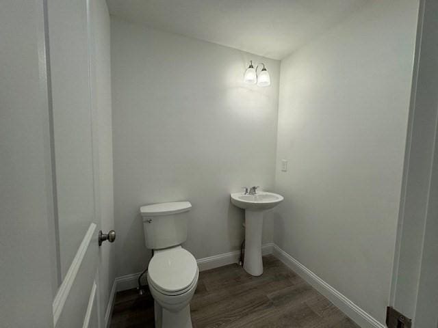 half bathroom with toilet, a sink, baseboards, and wood finished floors