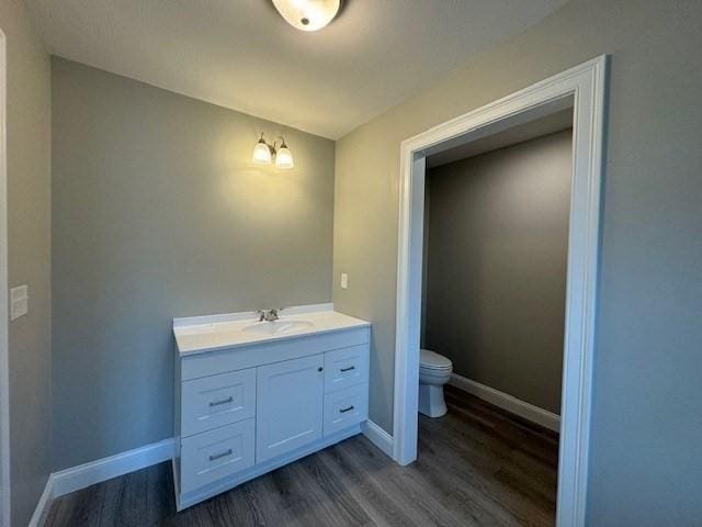 bathroom with toilet, baseboards, wood finished floors, and vanity