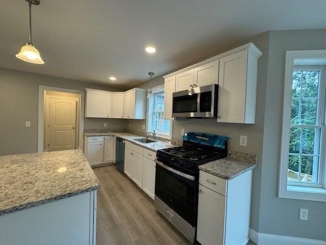 kitchen featuring gas range oven, stainless steel microwave, light wood-style flooring, white cabinets, and light stone countertops