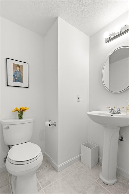 half bathroom featuring toilet, a textured ceiling, baseboards, and tile patterned flooring