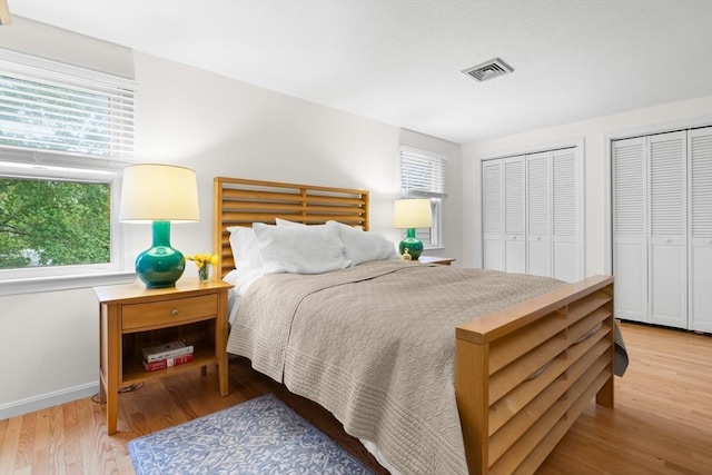 bedroom featuring multiple windows, light wood-style floors, two closets, and baseboards