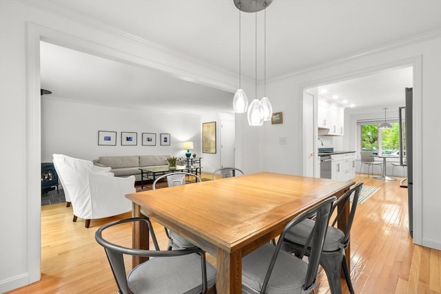 dining space featuring light wood-style floors, crown molding, and baseboards