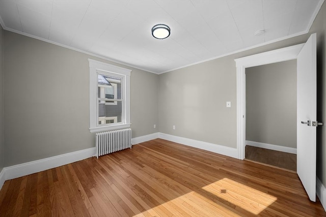 spare room with crown molding, radiator heating unit, baseboards, and wood finished floors