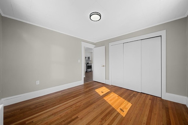 unfurnished bedroom featuring crown molding, wood finished floors, baseboards, and a closet