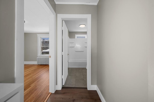 hallway with dark wood finished floors, crown molding, radiator heating unit, and baseboards