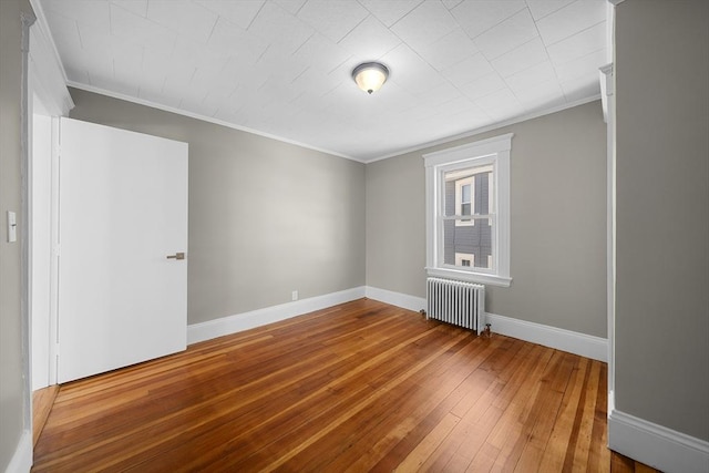 unfurnished room featuring radiator, baseboards, wood-type flooring, and ornamental molding