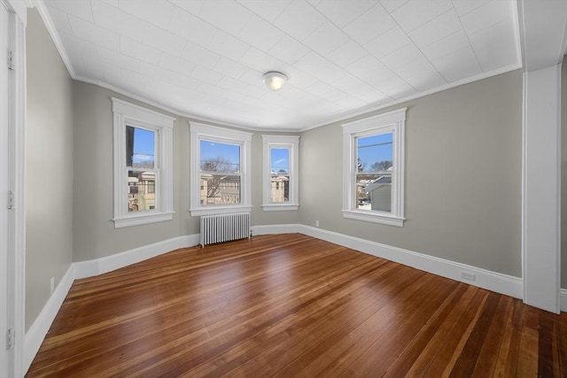 unfurnished room featuring baseboards, radiator, hardwood / wood-style floors, and crown molding