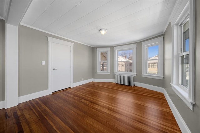 spare room with baseboards, wood-type flooring, radiator heating unit, and crown molding