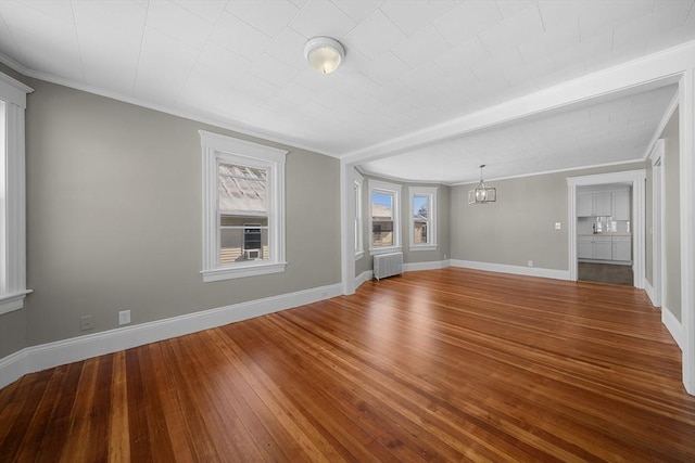 unfurnished living room featuring crown molding, radiator heating unit, wood finished floors, and baseboards