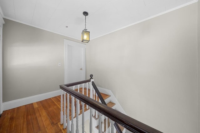 corridor featuring baseboards, an upstairs landing, wood-type flooring, and ornamental molding