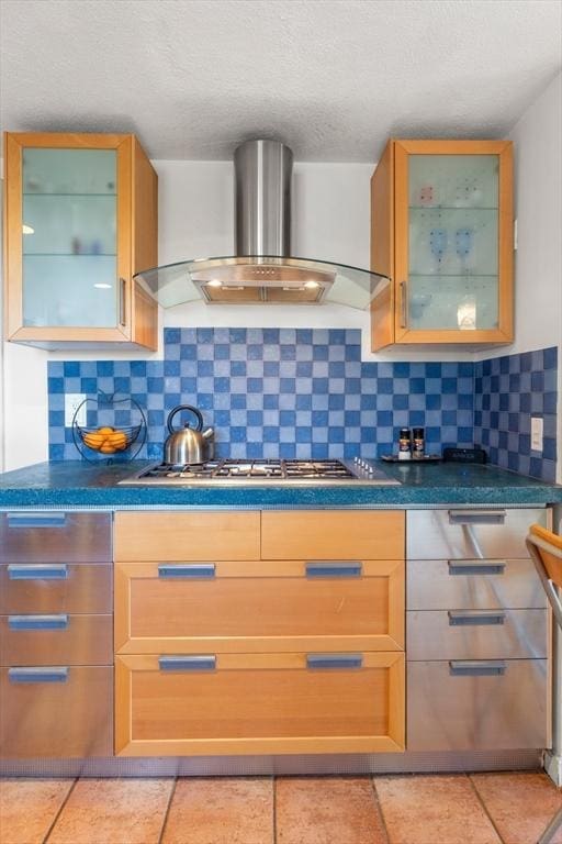 kitchen with glass insert cabinets, stainless steel gas stovetop, wall chimney range hood, and tasteful backsplash