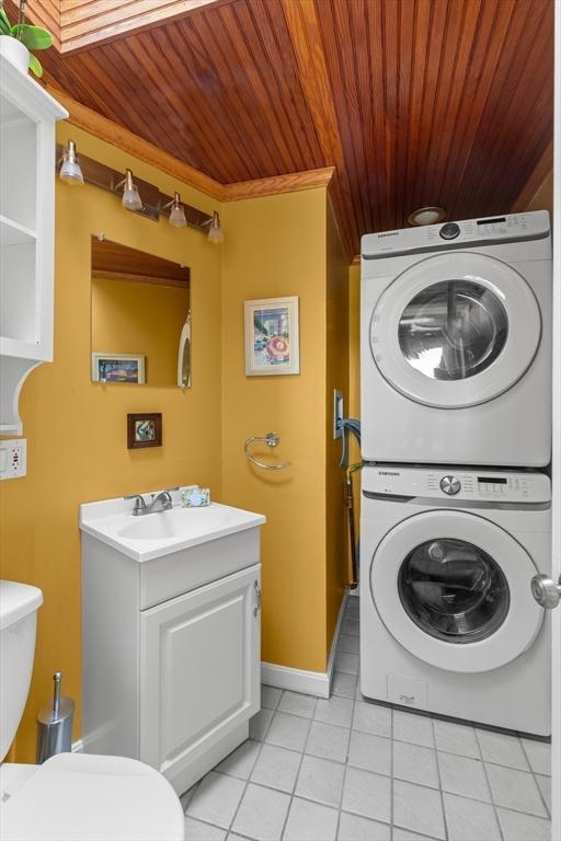 laundry area with a sink, stacked washing maching and dryer, light tile patterned floors, laundry area, and wood ceiling