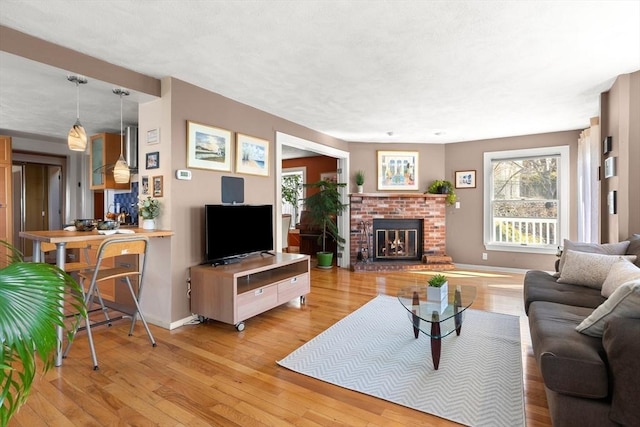 living area with a brick fireplace, a wealth of natural light, light wood finished floors, and baseboards