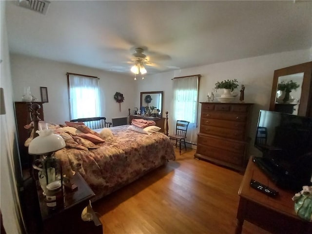 bedroom featuring wood finished floors, a baseboard heating unit, a ceiling fan, and visible vents