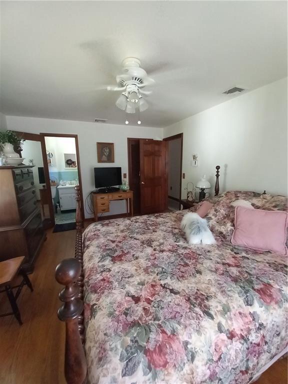 bedroom with wood finished floors, ceiling fan, visible vents, and connected bathroom