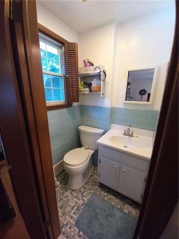 half bathroom featuring toilet, tile walls, vanity, wainscoting, and tile patterned flooring