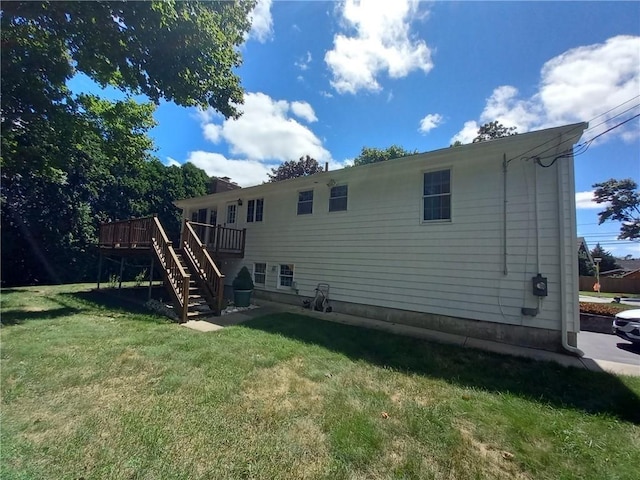 rear view of house featuring stairway, a wooden deck, and a lawn