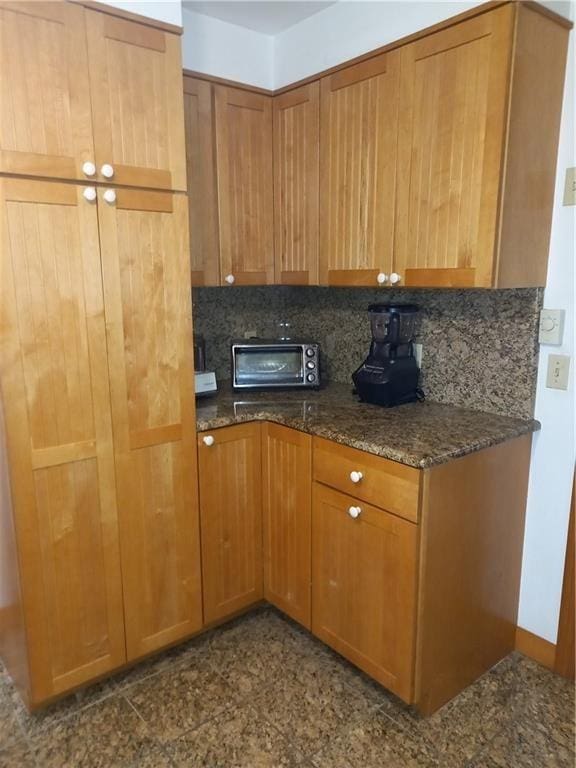 kitchen with brown cabinets, decorative backsplash, a toaster, and dark stone counters