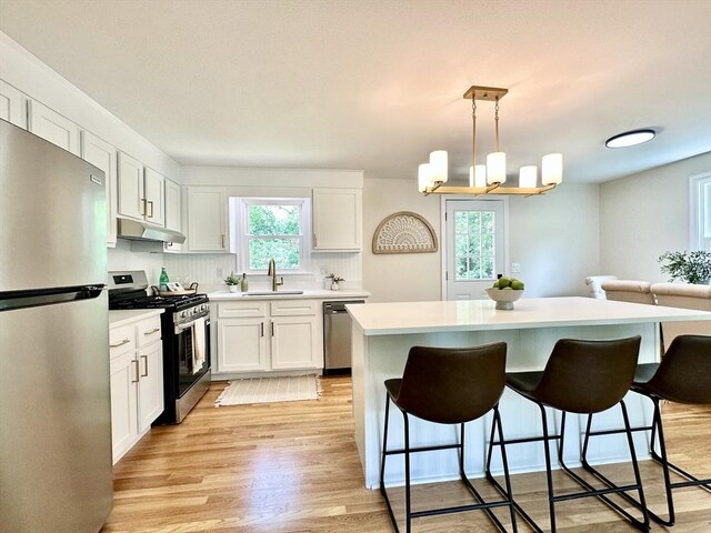 17 Kingsley Rd, Norton, MA 02766 - kitchen with appliances with stainless steel finishes, under cabinet range hood, a kitchen bar, light wood-type flooring, and white cabinetry
