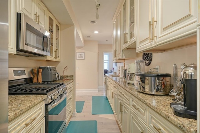 kitchen with stainless steel appliances, light stone countertops, and cream cabinetry