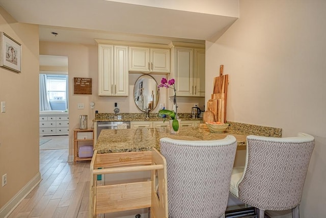 kitchen with light hardwood / wood-style flooring, light stone counters, kitchen peninsula, stainless steel dishwasher, and cream cabinetry