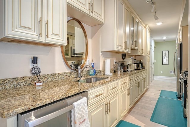 kitchen featuring sink, light stone counters, track lighting, appliances with stainless steel finishes, and light hardwood / wood-style floors