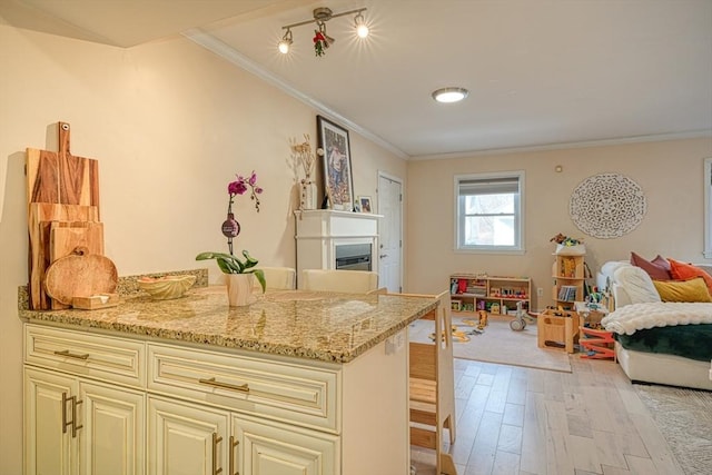 kitchen with light stone counters, ornamental molding, light hardwood / wood-style flooring, and cream cabinetry