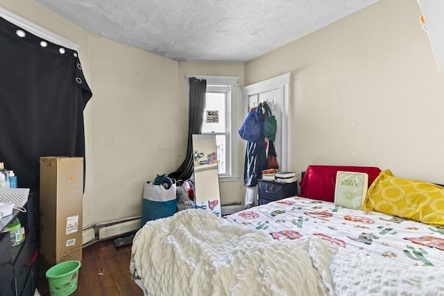 bedroom featuring baseboard heating, a textured ceiling, a closet, and dark hardwood / wood-style floors