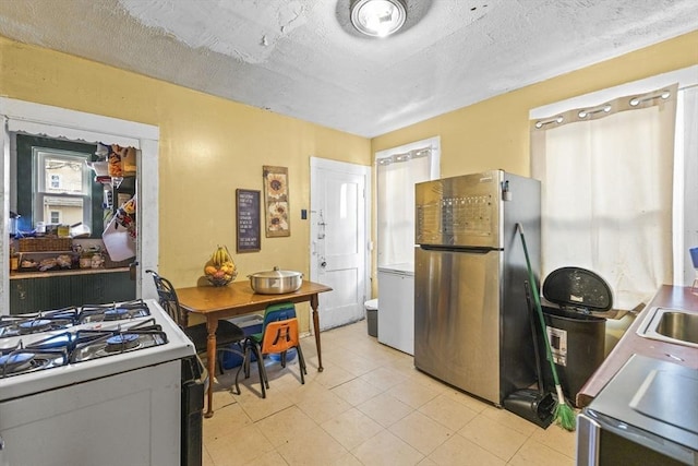 kitchen featuring sink, a textured ceiling, white range with gas stovetop, and stainless steel fridge