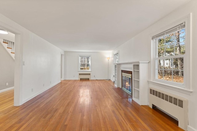 unfurnished living room with light wood-style flooring, a healthy amount of sunlight, and radiator heating unit