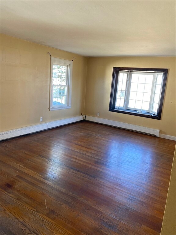 empty room with baseboard heating and dark hardwood / wood-style floors