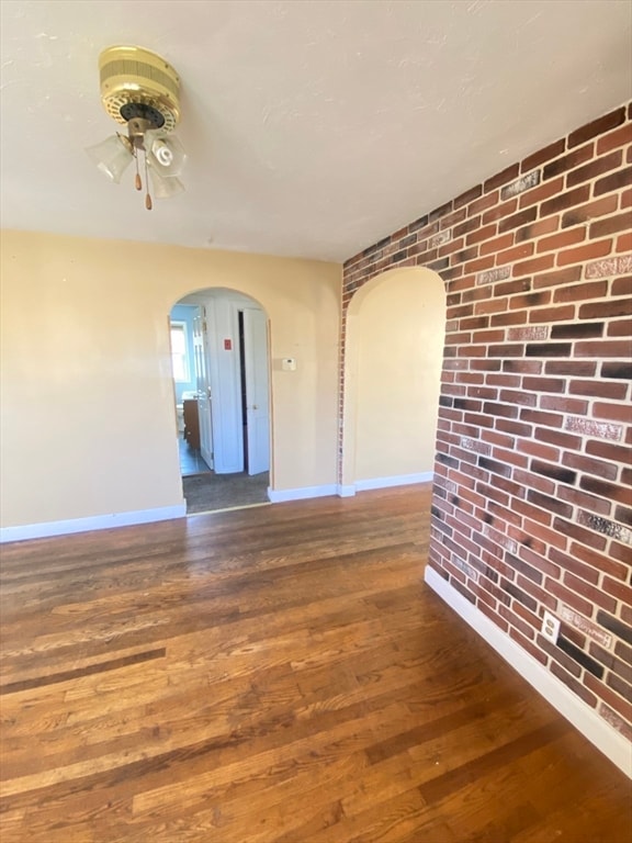 spare room with dark hardwood / wood-style flooring, ceiling fan, and brick wall