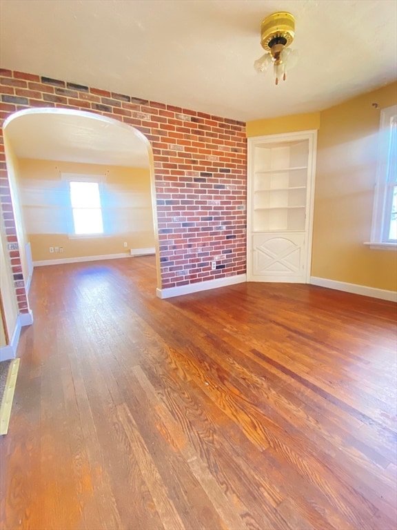 empty room featuring hardwood / wood-style flooring, built in shelves, and brick wall