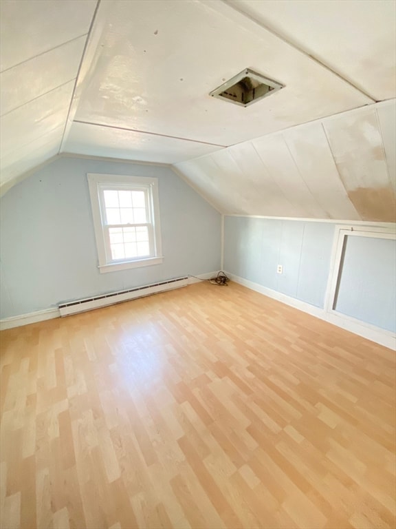 additional living space featuring light wood-type flooring, a baseboard radiator, and lofted ceiling