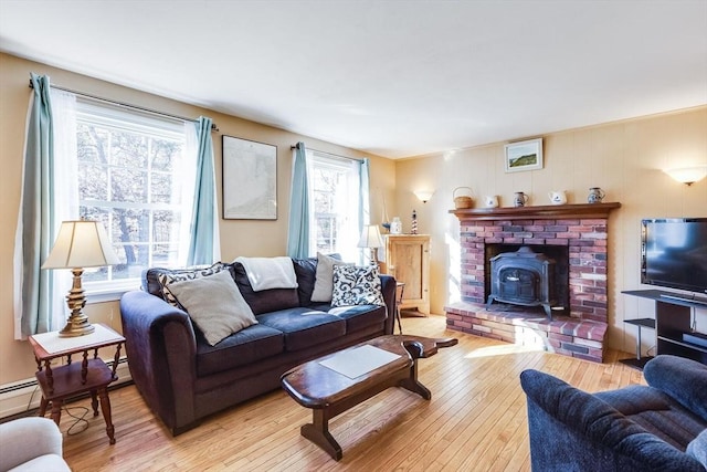 living room with a baseboard heating unit, a wood stove, and light hardwood / wood-style flooring