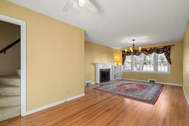 unfurnished living room featuring ceiling fan with notable chandelier and light hardwood / wood-style flooring