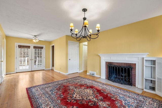 unfurnished living room with a fireplace, french doors, ceiling fan with notable chandelier, and hardwood / wood-style flooring