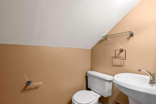 bathroom with toilet, vaulted ceiling, and sink