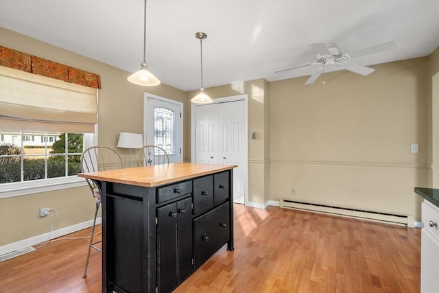 kitchen with pendant lighting, a breakfast bar, a center island, ceiling fan, and baseboard heating