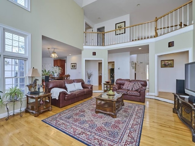 living area featuring a notable chandelier, a towering ceiling, baseboards, and wood finished floors