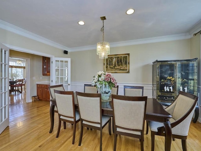 dining space with light wood-type flooring, a notable chandelier, wainscoting, and crown molding