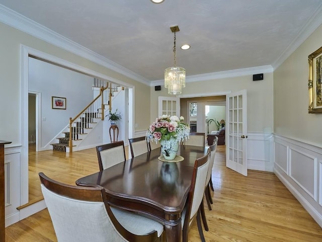 dining space with a wainscoted wall, crown molding, stairs, and light wood-type flooring