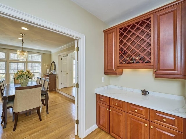 kitchen featuring pendant lighting, light wood-style flooring, brown cabinetry, baseboards, and a chandelier