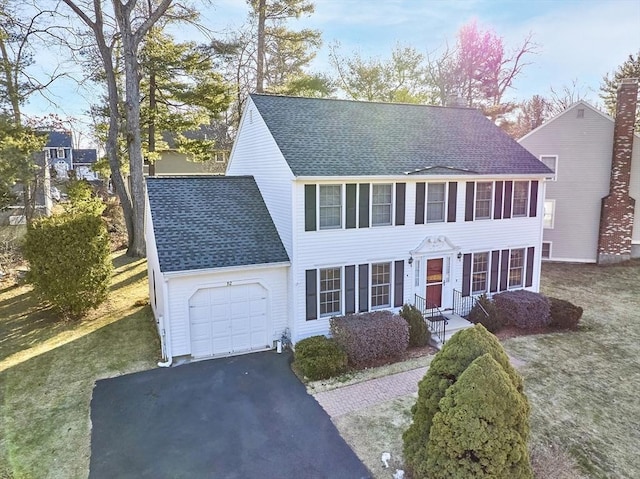 colonial inspired home with aphalt driveway, a front yard, a garage, and roof with shingles