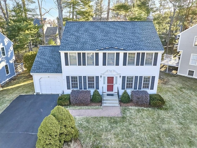 colonial-style house with a front yard, roof with shingles, a chimney, a garage, and aphalt driveway