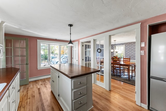 kitchen with a baseboard heating unit, light wood-type flooring, decorative light fixtures, white cabinets, and stainless steel refrigerator