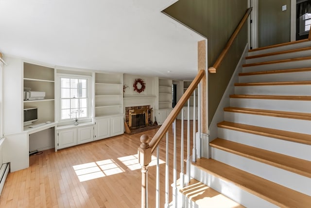 staircase with baseboard heating, a brick fireplace, and wood-type flooring