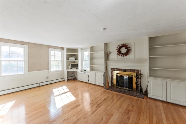 unfurnished living room featuring baseboard heating, built in shelves, and light wood-type flooring