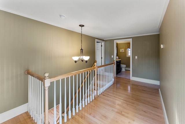 hall with crown molding, wood-type flooring, an inviting chandelier, and a baseboard heating unit